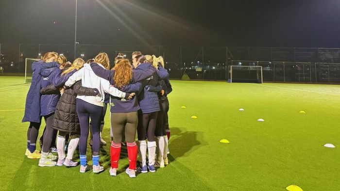 A group of girls huddled in a circle on a hockey pitch